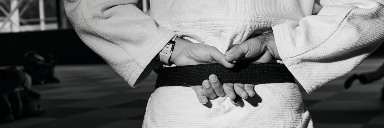 Eine Detailaufnahme von den Haenden eines Judoka, die hinter seinem Ruecken den schwarzen Guertel umfassen.